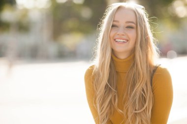 Çekici, genç, sarışın kadın portresi. Sonbahar güneşinin arka planında açık havada bir kadın. Sonbaharda neşeli bir kadın portresi..