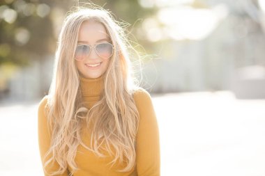 Çekici, genç, sarışın kadın portresi. Sonbahar güneşinin arka planında açık havada bir kadın. Sonbaharda neşeli bir kadın portresi..