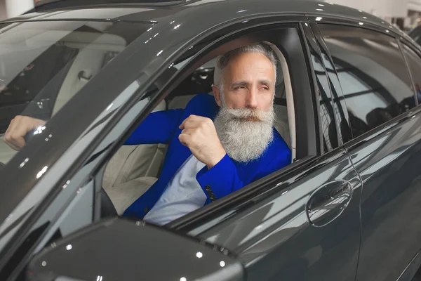 Old stylish man in car sales center. Mature man choosing new automobile.