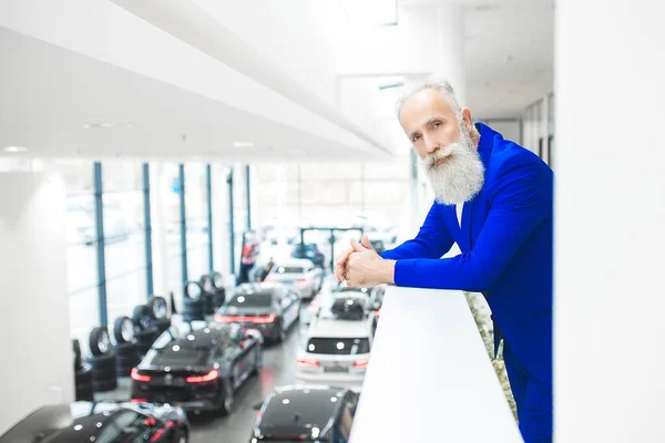 Old stylish man in car sales center. Mature man choosing new automobile.