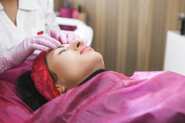 Cosmetologist making a face massage to her patient and a face mask. Anti-ageing and smoothing procedure in a beauty salon. Doctor in a cosmetological clinic making a treatment of skin care clipart