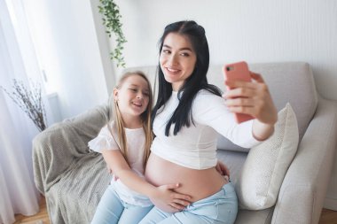 Anne ve küçük kızı birlikte selfie çekiyorlar. Anne ve çocuk evde akıllı telefonla fotoğraf çekiyorlar..