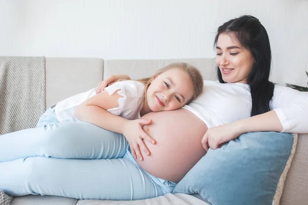 Young pregnant mother and her little daughter indoors. Child and her mom waiting for a little new born baby. Happy family expecting.