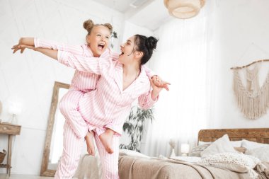 Genç aktif anne ve küçük kızı evde pijama giyerek eğleniyorlar.