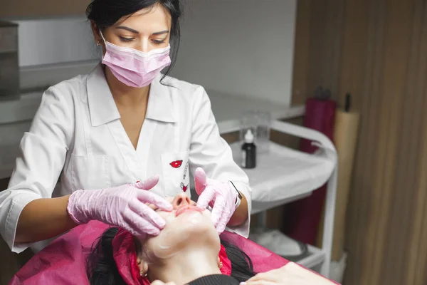 Cosmetologist making a face massage to her patient and a face mask. Anti-ageing and smoothing procedure in a beauty salon. Doctor in a cosmetological clinic making a treatment of skin care