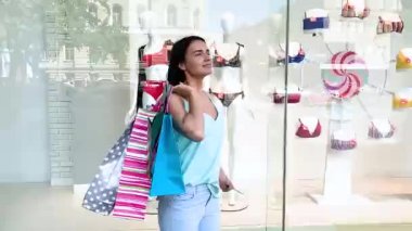 Vitrinin yanında alışveriş torbaları taşıyan çekici bir kadın..