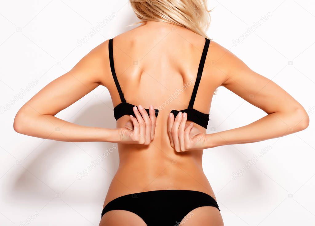 rear view of young woman taking off her bra on white background