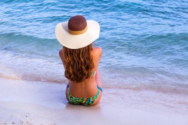 kumsalda oturuyor ve tatil zevk şapkalı genç kızın arka görünüm