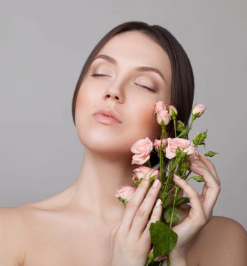 Doğal makyaj ve kapalı gözler gri arka plan üzerinde güllü poz olan hassas kadın portresi 