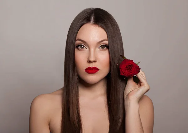 年轻的女人与红色的嘴唇摆姿势与红色玫瑰在灰色的背景 — 图库照片