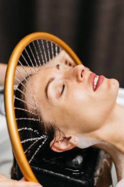 Hidroterapi gören bir kadın, başından aşağı su akarken rahatlatıcı bir spa ortamında rahatlamayı ve sağlığını destekliyor, su masajı terapisinin faydalarını vurguluyor.