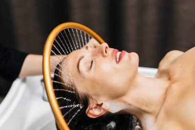 Sakin bir spa ortamında hidroterapi gören bir kadın, kafasının üzerinden yumuşak su akıyor, rahatlatıcı bir atmosfer yaratıyor bu da su masajı yoluyla rahatlık ve sağlığını arttırıyor.