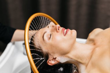 Sakin bir spa ortamında hidroterapi gören bir kadın kafasından aşağı su akarken, yenilikçi su masajı yöntemleri ve rahatlatıcı atmosfer yoluyla rahatlık ve sağlığını geliştirir.