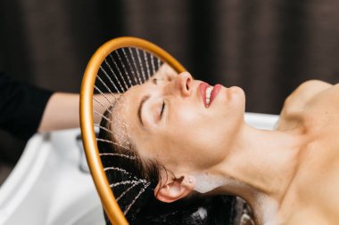 Sakin bir spa ortamında hidroterapi gören bir kadın kafasından aşağı su akarken, yenilikçi su masaj yöntemleriyle rahatlama ve sağlığını geliştirir.