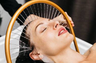 Sakin bir spa ortamında hidroterapi gören bir kadın, kafasından aşağı doğru süzülen su, yenilikçi su masajı yöntemleri ve rahatlatıcı atmosfer yoluyla rahatlık ve sağlığını arttırıyor.