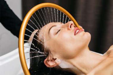 Sakin bir spa ortamında hidroterapi gören bir kadın, başından aşağı yavaşça akan su, rahatlatıcı bir atmosferde su masajı ve tedavisel su tedavisi ile rahatlama ve sağlığını arttırıyor.