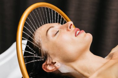 Sakin bir spa ortamında hidroterapi gören bir kadın, başının üzerinden yavaşça akan su, rahatlatıcı su masajı teknikleri ve dingin ortam yoluyla rahatlık ve sağlığını arttırıyor.