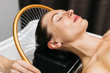 Sakin bir spa ortamında hidroterapi gören bir kadın kafasından aşağı su akarken, yenilikçi su masajı yöntemleri ve rahatlatıcı atmosfer yoluyla rahatlık ve sağlığını geliştirir.