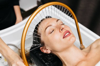 Sakin bir spa ortamında hidroterapi gören bir kadın, kafasından aşağı doğru süzülen su, yenilikçi su masajı yöntemleri ve rahatlatıcı atmosfer yoluyla rahatlık ve sağlığını arttırıyor.