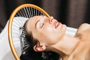 Kadın bir hidroterapi terapisi seansına dalmış, sakin bir spa ortamında başının üstünde hafif su akıntıları yaşıyor, rahatlatıcı su masaj yöntemleriyle rahatlık ve sağlığını arttırıyor.