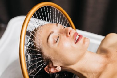 Sakin bir spa ortamında hidroterapi gören bir kadın, başının üzerinden yavaşça akan su, su terapisi teknikleriyle rahatlatıcı bir atmosfer yaratıyor.