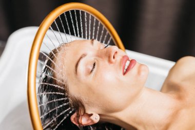 Kadın su masajı terapisine dalmış, dairesel bir armatürden akan su, kaplıca ortamında dingin bir atmosfer yaratıyor, su masajı yoluyla rahatlama ve gençleşme vurguluyor.