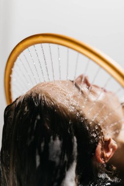 Hidroterapi gören bir kadın, yenilikçi bir su masajı cihazı ile saçlarının üzerinde çağlayan su, sakinlik ve sakinlikle dolu rahatlatıcı bir spa ortamında rahatlığı arttırıyor.