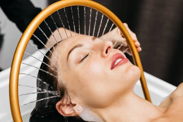 Sakin bir spa ortamında hidroterapi gören bir kadın, kafasından aşağı doğru süzülen su, yenilikçi su masajı yöntemleri ve rahatlatıcı atmosfer yoluyla rahatlık ve sağlığını arttırıyor.