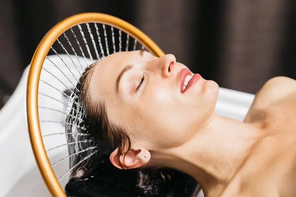 Kadın bir hidroterapi terapisi seansına dalmış, sakin bir spa ortamında başının üstünde hafif su akıntıları yaşıyor, rahatlatıcı su masaj yöntemleriyle rahatlık ve sağlığını arttırıyor.