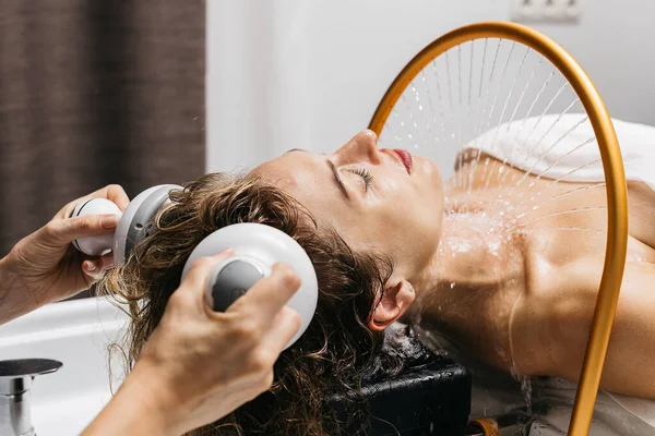 Kadın, Japon spa merkezinde hidromasaj yaptırmayı seviyor, su yavaşça akıyor, kafa derisine masaj aleti uygulanıyor, rahatlama ve gençleşme deneyimi sırasında sakin bir ortam yaratıyor.