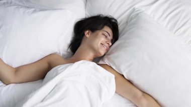 Gülümseyen kadın beyaz bir yatakta uyanıyor.