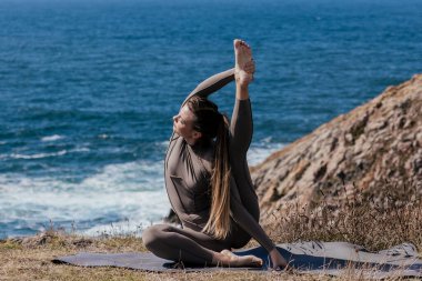 Dişi yogi, kayalık araziyle çevrili okyanus kıyısındaki bir paspas üzerinde esneyerek doğayla bir barış anı ve bağlantı kurar.