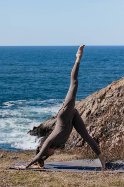 Dişi yogi, okyanus kenarındaki bir mindere eğilip sakin bir sahil ortamında gücünü ve esnekliğini ön plana çıkarıyor.