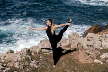 Kadın meditasyon yapıyor ve kayalık kıyılarda geriniyor. Etrafı okyanus dalgalarıyla çevrili. Denge, sükunet ve doğa ile bağlantı kuruyor.