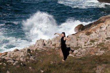 Kayalık kıyılarda esneme ve meditasyon yapan bir kadın figürü. Yakınlarda okyanus dalgaları çakılıyor. Huzurlu ve huzurlu bir atmosfer yaratıyor.