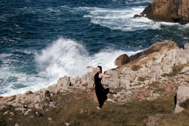 Kayalık kıyılarda esneme ve meditasyon yapan kadın figürü, çarpan dalgalar ve doğal güzelliklerle çevrili, açık havada barışı ve farkındalığı teşvik ediyor.