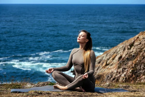 Dişi yogi, okyanus dalgaları ve kayalık bir ortamda huzur verici bir atmosfer yaratarak, huzurlu bir açık havada bir minder üzerinde meditasyon yapıyor.