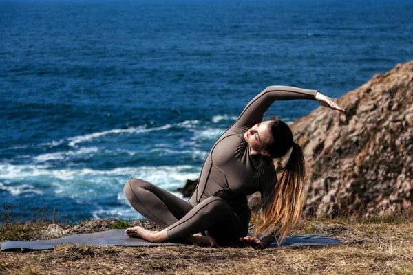 Dişi yogi okyanus kıyısındaki bir mindere geriliyor, arka planda dalgalar çarpıyor, meditasyon ve rahatlama için huzurlu bir atmosfer yaratıyor.