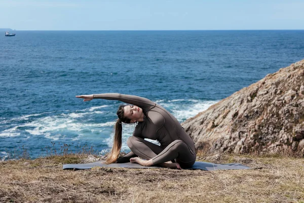 Dişi yogi, okyanusun kenarındaki bir mindere uzanıyor, doğayı ve sükuneti kucaklıyor, arka planda dalgalar çarpıyor, barışçıl atmosferi güçlendiriyor.
