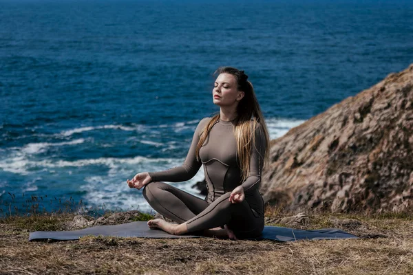 Dişi yogi okyanus kıyısındaki bir minder üzerinde meditasyon yapıyor. Arka planda dalgalar var. Rahatlamak ve kendini keşfetmek için huzurlu bir atmosfer yaratıyor.