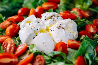 Çeri domates ve yeşilliklerle çevrili taze burrata peyniri.