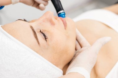 Kadın müşteri çağdaş bir kozmetoloji ortamında hidrakiyal tedaviden, cilt bakım araçlarından ve etkili bir yüz yenileme için rahatlatıcı bir atmosferden hoşlanır.