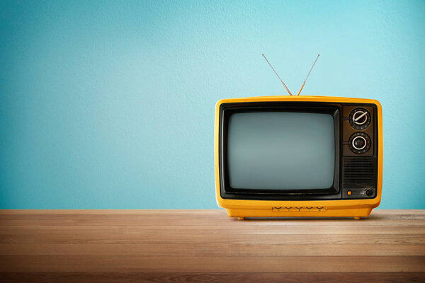 Yellow Orange color old vintage retro Television on wood table with mint blue background