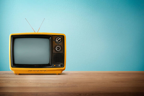 Yellow Orange color old vintage retro Television on wood table with mint blue background