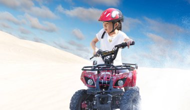 Küçük kız güzel mavi ve beyaz gökyüzü ile çölde ATV quad bisiklet sürme .