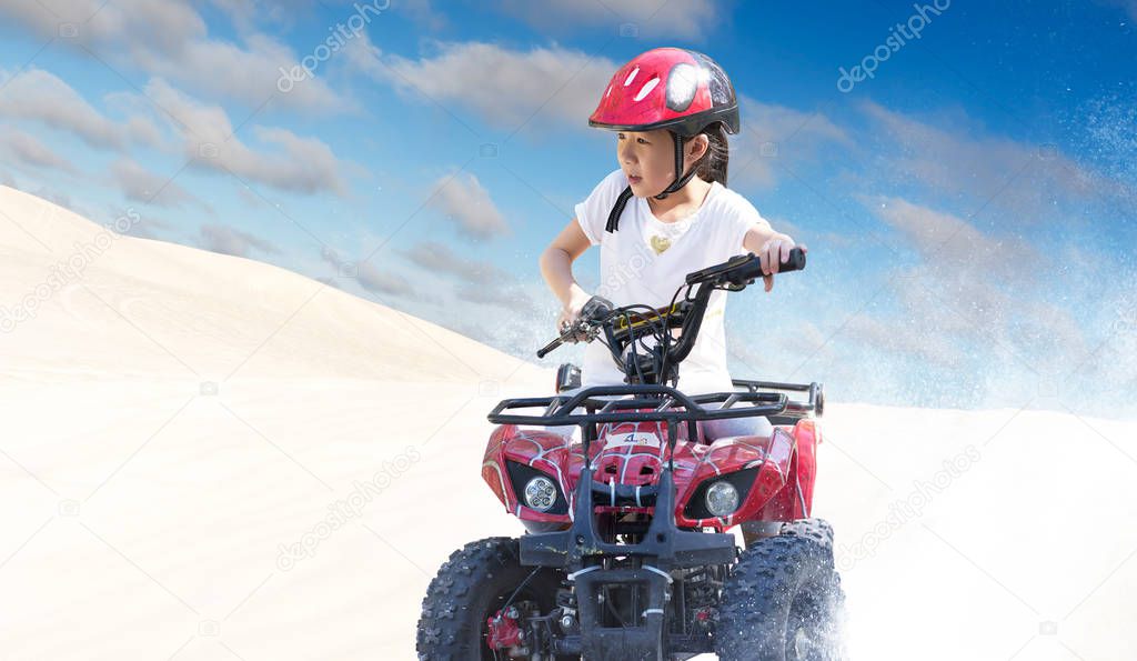 Little girl riding ATV quad bike in desert with beautiful blue and white sky .