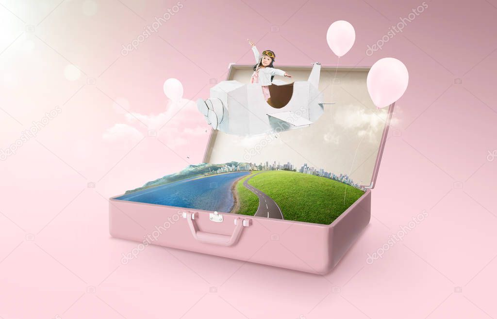 Little asian girl enjoy with fantasy cardboard plane fly and floating in an open retro vintage suitcase isolated on pink background . Travel and vacation concept.