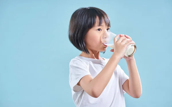 可爱聪明的亚洲小女孩喝牛奶在蓝色背景 — 图库照片
