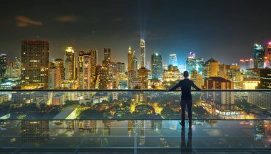 Gece şehir panoramik manzaralı, saydam cam zemin üzerinde duran bir işadamı..