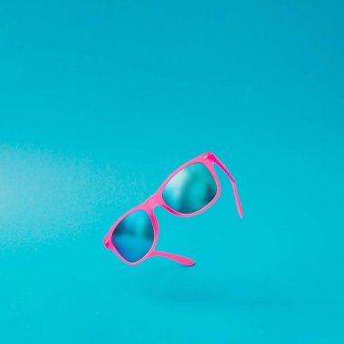 Pastel mavi arka plan, en az yaz kavramı üzerinde pembe güneş gözlüğü 